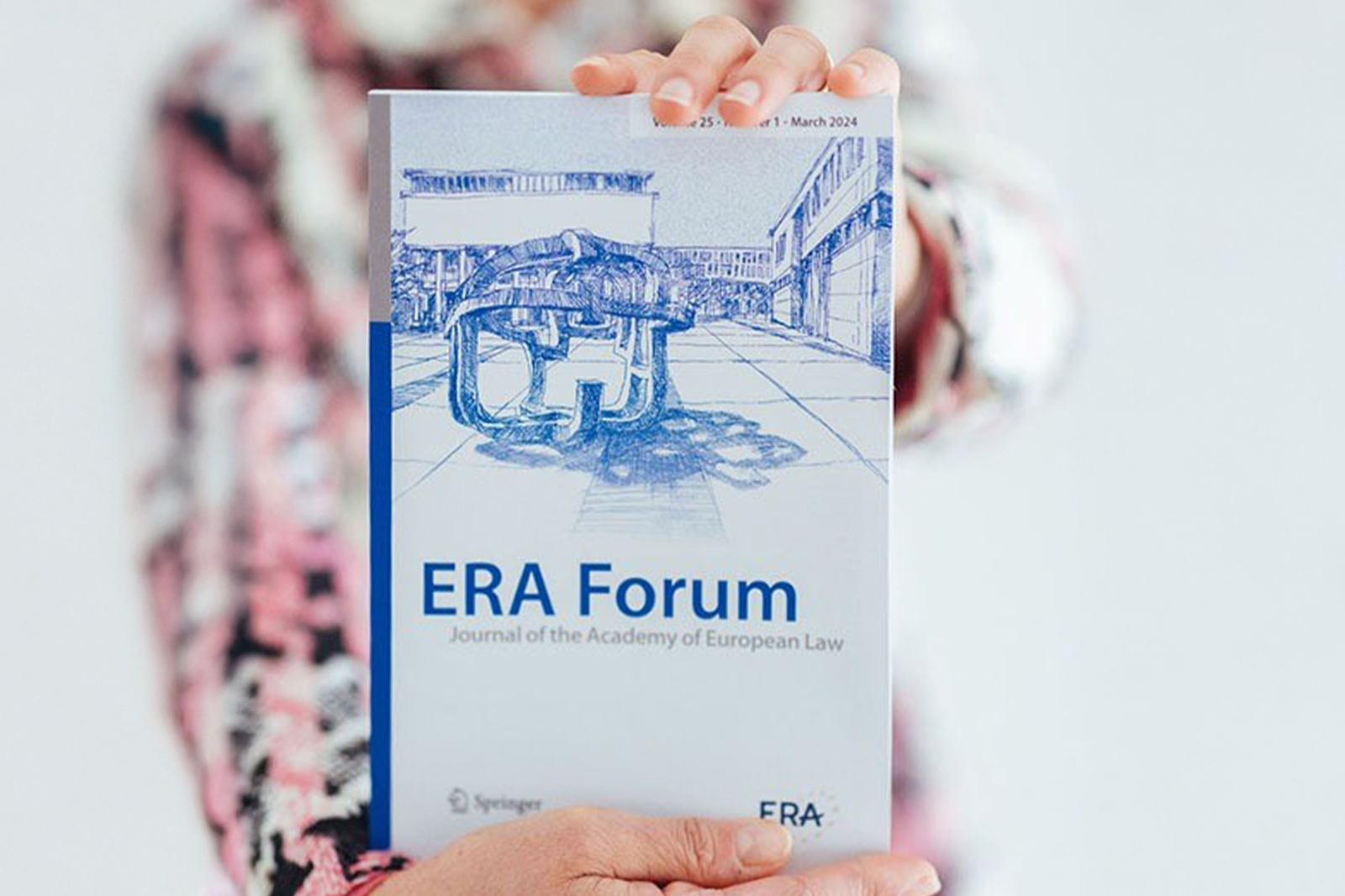 A person holds up the latest issue of the ERA Forum – Journal of the Academy of European Law. The cover features a blue sketch of the ERA building, symbolising the successful launch of the quarterly ERA Forum Journal in March 2024.